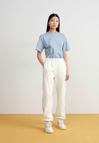 Modrá bavlnená tričko v kombinácii s bielymi flísovými teplákmi so bočnými pruhmi. Bielé tenisky zvýrazňujú neformálny outfit.