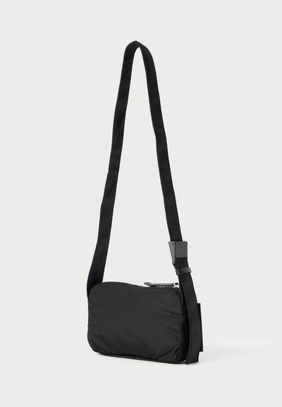 Mala de ombro preta feita de nylon texturizado, com alça ajustável, formato retangular e fecho com zíper. Adequada para uso casual.