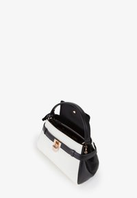 Borsa strutturata con base in pelle nera e corpo in tela bianca. Dettagli in oro sulla parte frontale e chiusura superiore a cerniera.