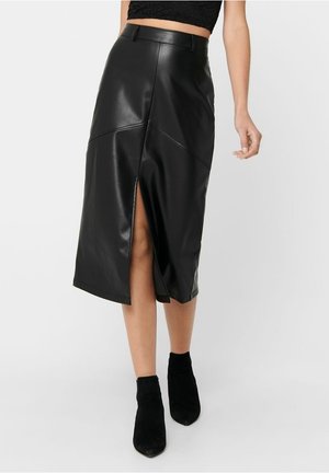 Czarna skórzana spódnica z przednim rozcięciem, z ukośnymi szwami i gładką fakturą. Widoczny pas w talii, zestawiona z czarnymi botkami do kostki.