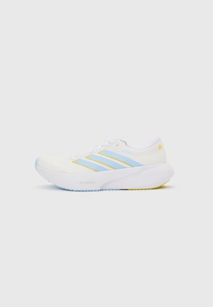 Λευκό αθλητικό παπούτσι με ανοιχτό μπλε ρίγες και κίτρινες λεπτομέρειες, χοντρή λευκή σόλα, εμφανίζεται σε προφίλ πλευρικής όψης σε απλό φόντο.