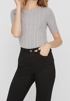 Grå ribbet striktrøje med korte ærmer og bølget udsnit ved halsen, parret med højtaljede sorte jeans med forlommer og knaplukning.