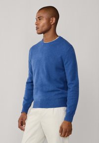 Bl�å tröja i mjukt tyg med rundad halsringning och ribbade ärmändar. Designad med en figurnära passform och minimal struktur, kombinerad med krämfärgade byxor.