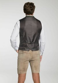 Dunkelgraue Weste mit strukturierter Oberfläche, ausgestattet mit einem Hinterriemen, kombiniert mit hellbraunen Shorts. Sichtbare Nähte und Knopfdetails.