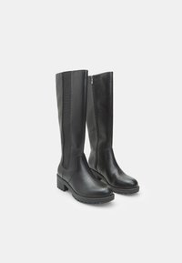 Stivali in pelle neri al ginocchio con tacco basso e robusto, zip laterale su uno stivale e pannello elastico sull'altro per una vestibilità regolabile.