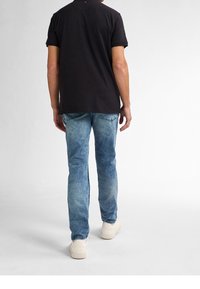 Svart t-shirt med kort ärm som är kombinerad med ljusblå, urtvättad jeans och vita sneakers, sedd från baksidan. Enkel design utan synliga logotyper.