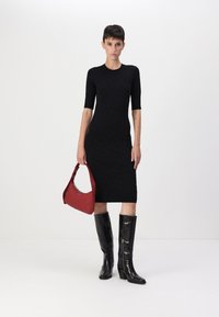 Abito aderente nero con maniche corte, tessuto texturizzato; modella che tiene una borsa rossa, indossando stivali neri al ginocchio con finitura lucida.