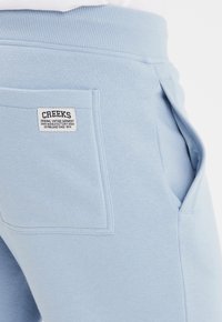 Lichtblauwe sweats met een geribbelde tailleband, zijzakken en een vierkante labelpatch die op de achterzak is genaaid. Zacht katoen materiaal.