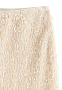 Beige texturerad kjol prydd med spridda, cirkulära paljetter. Har ett mjukt, vågigt tyg som tillför dimension till designen.