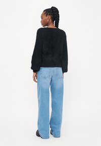 Zwarte donzige trui met lange mouwen, gecombineerd met lichtblauwe wijde jeans en zwarte platform schoenen. Zachte textuur en relaxte pasvorm.