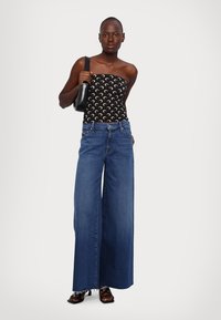 Haut noir sans bretelles avec motif de croissant de lune, associé à un jean bleu à jambes larges, en denim texturé, et des sandales à talons hauts. Accessoire : sac à main noir.