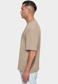 Camiseta de algodón beige con mangas cortas y un corte relajado, que presenta un logo sutil en el frontal y un dobladillo recto.