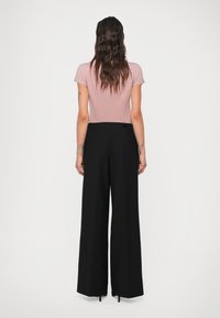 Camiseta ajustada de color rosa pálido combinada con pantalones de pierna ancha negros de talle alto. Textura distintiva y tejido suave, con una marca mínima en la cinturilla.