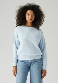 Helleblaue Sweatshirt aus weichem Material, mit Rundhalsausschnitt, langen Ärmeln sowie Rippbündchen und -saum. Kombiniert mit hellen Denim-Jeans.