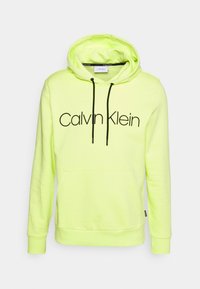 Felpa con cappuccio Calvin Klein giallo neon con logo nero, coulisse, tasca a marsupio frontale e polsini a coste. Morbido materiale in misto cotone.