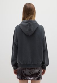 Felpa con cappuccio grigio scuro dalla vestibilità ampia e spalle scese, abbinata a una minigonna luccicante con paillettes. Tessuto liscio, design casual.