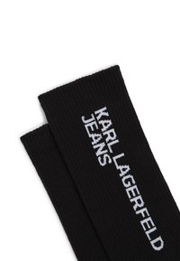 Svarta ribbade strumpor med texten "KARL LAGERFELD JEANS" i vitt, placerad i närheten av toppen. Tillverkade av ett texturerat stickat material.