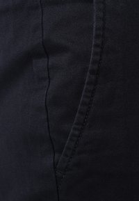 Czarne dżinsowe spodnie z boczną kieszenią, gładką teksturą i lekkim połyskiem, z widocznym szwem wzdłuż szwów.