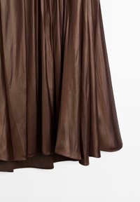 Hnědá plisovaná sukně z lesklé, hladké látky s plynulým střihem a lemem elegantně sahajícím pod kolena.