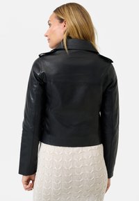 Giubbotto di pelle nera con un design aderente e una morbida texture, dotato di colletto a punta e sottili epaulettes sulle spalle.