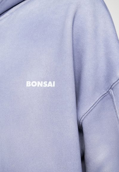 Lavandas džemperis ar mīkstu tekstūru, uz priekšpuses ir balts "BONSAI" logo. Tam ir brīvs piegriezums un ribotas piedurknes.