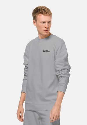 Sweatshirt gris en tissu doux, doté de manches longues, d'un col rond et d'un petit logo noir sur le côté supérieur gauche de la poitrine.