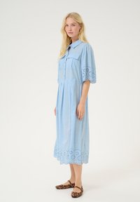 Svetlo modra srajčna obleka s kratkimi nabranimi rokavi, dvema sprednjima žepoma, zapletenim čipkastim obrobom in vezenimi cvetličnimi detajli. Uporabljena z balerinkami v leopardjem vzorcu.