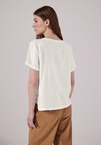 T-shirt bianca a maniche corte con vestibilità rilassata, con scollatura rotonda e polsini arrotolati. Texture morbida, design minimale, senza pattern visibili.
