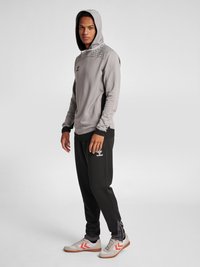 Grijze hoodie met een gestructureerde schouderpartij, zwarte taps toelopende broek en grijze sneakers met rode accenten en een logo op de zijkant.