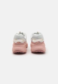 Witte en roze sport schoenen met een gestructureerde zool, een gewatteerde kraag en een trekband, met een gladde bovenkant en contrasterende accenten.