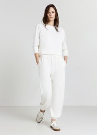 Weißer Pullover mit einem verkürzten Design und langen Ärmeln, kombiniert mit lockeren weißen Hosen mit elastischem Bund und Seitentaschen.