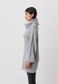 Szary, dziany, oversize sweter z golfem, o prążkowanej fakturze i luźnym kroju, noszony na czarnych skórzanych spodniach.