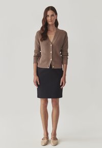 Beige neulecardigan, jossa on V-pääntie ja puunapit, yhdistetty tummansiniiseen kynähameeseen, jossa on pieniä pilkkukuviota.