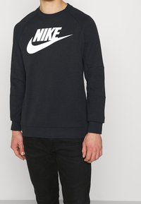 Mörkgrå Nike-tröja med vitt logotyp, rund halsringning och raglanärmar. Tillverkad av mjukt tyg med ribbade avslut och cuffs, minimalistisch design.