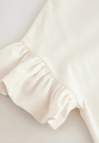 Weißer Baumwollhemdsaum mit Rüschendetails, der eine weiche, glatte Textur und subtile Falten aufweist, die das Gesamtdesign des Kleidungsstücks verbessern.