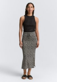 Haut sans manches noir avec un éclat, associé à une jupe de longueur mi-genoux avec un motif de grille blanche et une fente sur le côté. Porté avec des sandales noires.
