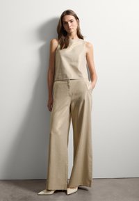 Top sans manches en lin beige avec une silhouette droite, associé à un pantalon large de couleur assortie. Des chaussures beige pointues complètent le look.