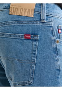 Primer plano del bolsillo trasero de unos vaqueros de mezclilla azul claro con etiquetas de la marca Big Star en rojo y un diseño de montaña bordado.