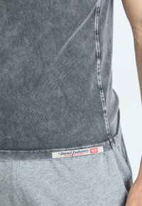 Grå tanktop med en falmet tekstur, som har et synligt sømdetalje og et mærke med "Diesel Industry" på en grå talje.