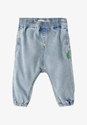 Jean pour tout-petit bleu clair avec taille élastique et ourlet resserré, poches latérales et petite étiquette en tissu verte sur la jambe droite.