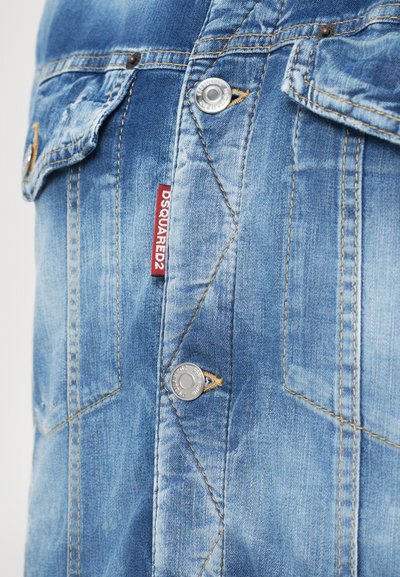 Heleda sinine denim jakk kahe rinnataskuga, hõbedased nupud, kollased õmblused ja ees punane DSquared2 silt.