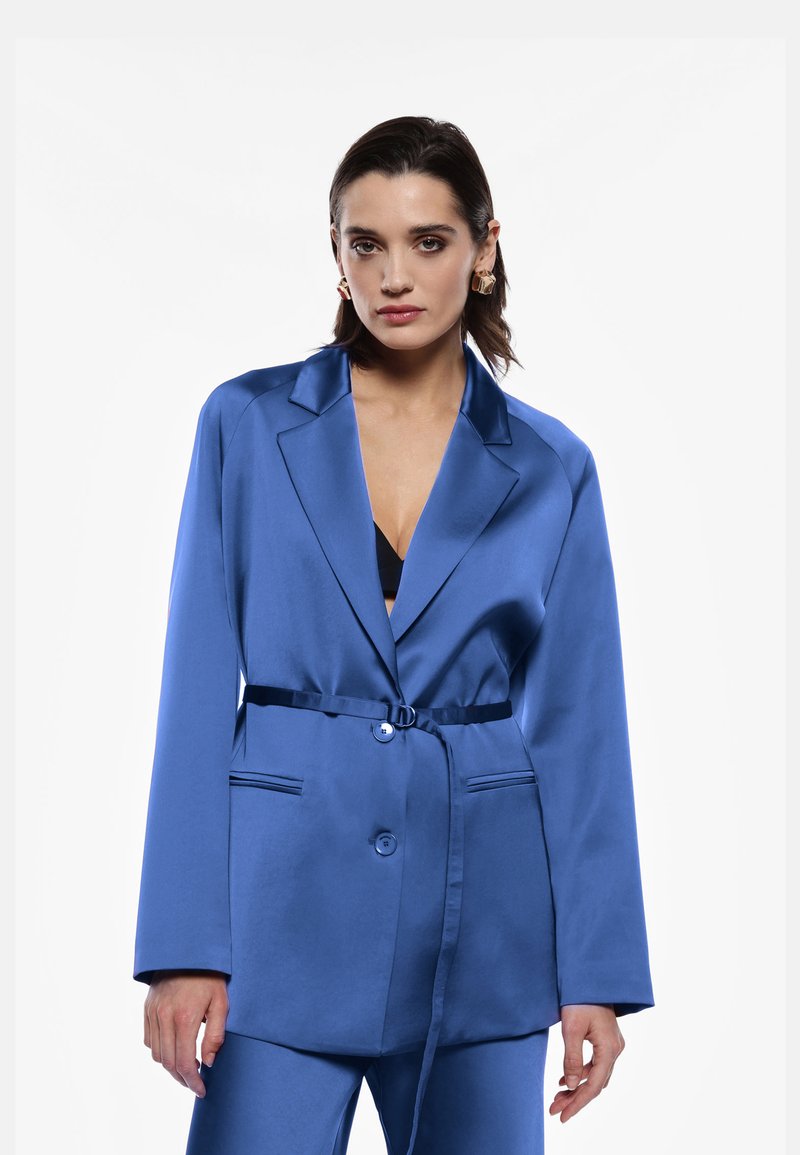 Blazer satin blu con rever a punta, chiusura con un solo bottone, tasche laterali e cintura coordinata. Texture liscia ed design elegante.