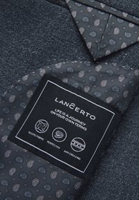 Ciemnoniebieska tkanina o teksturowej powierzchni. Wewnętrzna podszewka ma wzór paisley. Metka informuje: "LANCERTO. Tkanina elastyczna. Idealne dopasowanie. Antygnieceniowa."