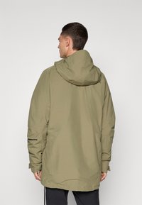 Olívazöld, vízálló parka kabát kapucnival, laza szabással, két oldalsó zsebbel és fekete részletekkel.