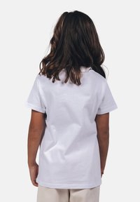 Camiseta de algodón blanca con mangas cortas, diseño simple, escote redondo, textura suave y un pequeño gráfico negro en la parte de atrás.