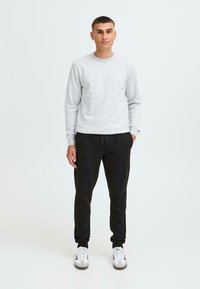 Grau sweatshirt mit Rundhalsausschnitt, kombiniert mit schwarzen Jogginghosen. Das Outfit hat ein lässiges Design und wird durch weiße Sneakers ergänzt.