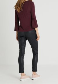 Burgundy bell-sleeve top paired with fitted black faux leather pants and light pink sneakers, showcasing a casual outfit design.