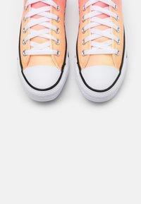 Różowo-pomarańczowe trampki z gradientowym wzorem na płótnie, z białym, gumowym czubkiem, sznurowanym zapięciem i czarnymi akcentami na podeszwie.