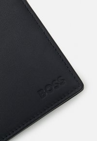 Black leather wallet corner with embossed "BOSS" logo, featuring a smooth texture and clean stitching along the edge.
