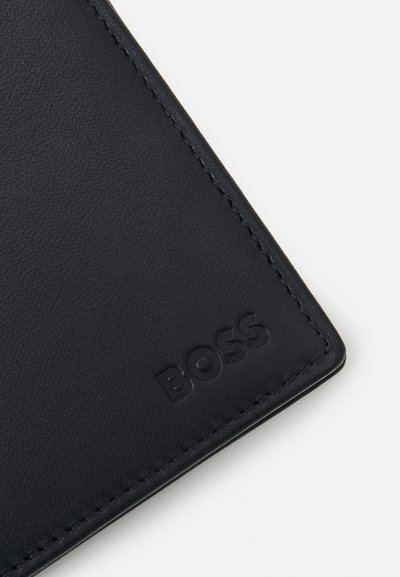 Porte-monnaie en cuir noir avec un coin embossé du logo "BOSS", présentant une texture lisse et des coutures nettes le long du bord.